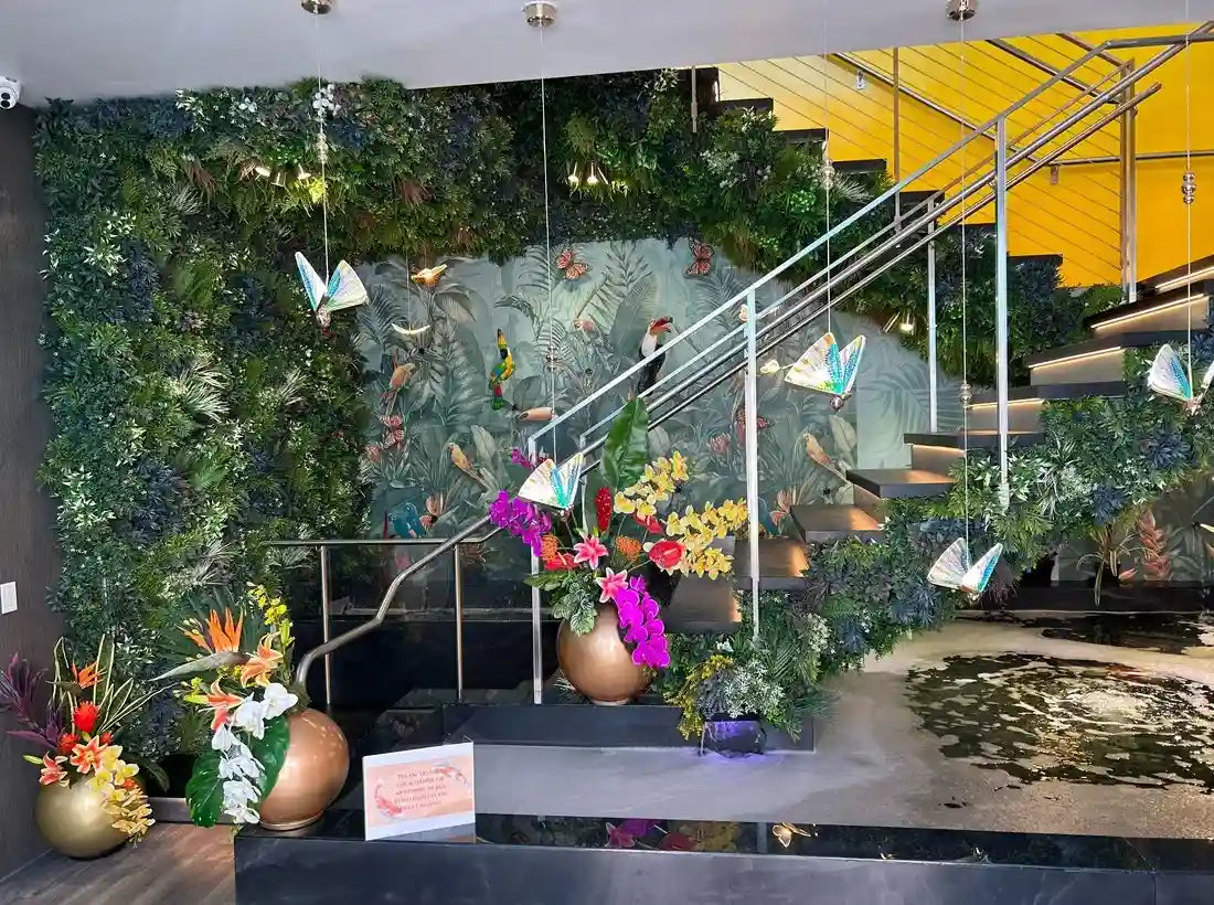 Tropical artificial green wall with hanging butterfly decor bird mural and orchid arrangement by stair railing