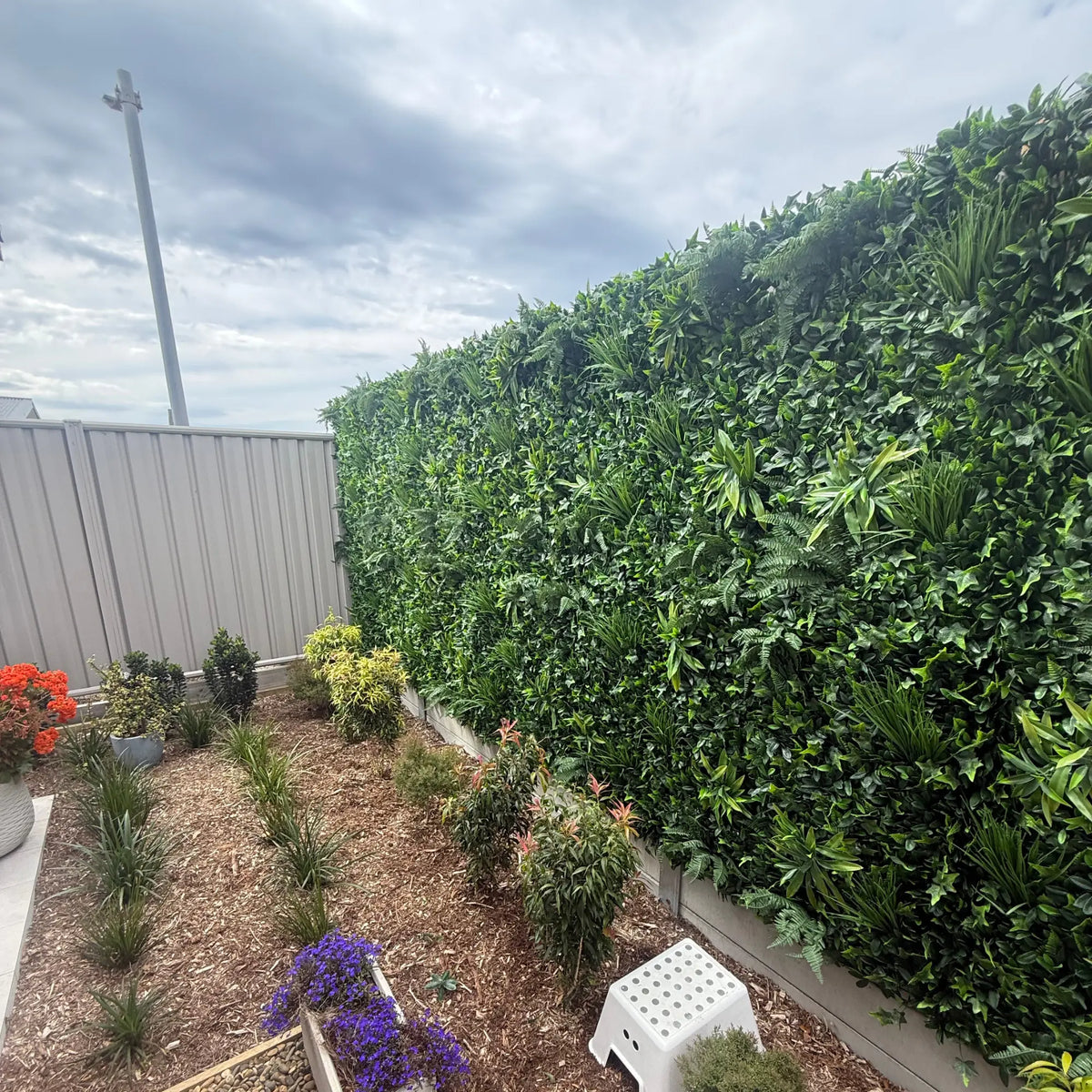 Artificial green plant privacy hedge wall in modern backyard garden setting.