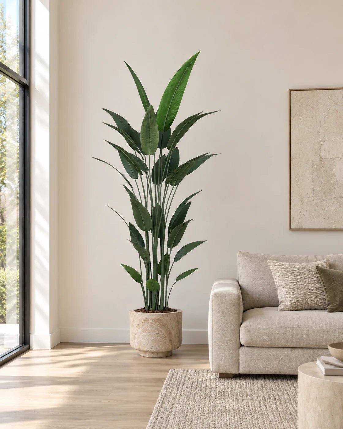 210 cm artificial Bird of Paradise in a marble-effect pedestal planter beside a linen sofa in a naturally lit living room.