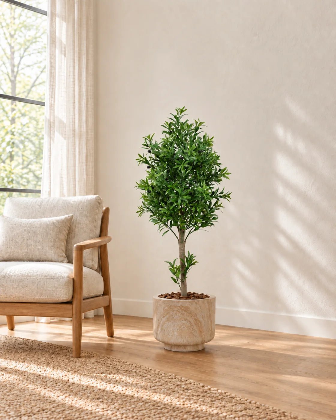 120 cm artificial olive tree styled in a marble-effect pedestal planter beside a cream armchair in a sunlit living room.