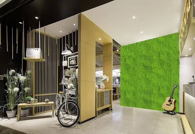 An outdoor room with a green wall adorned with a Faux Evergreen Moss Mat 5.5 SQFT UV Resistant Commercial Grade UV Resistant panels and a bicycle.