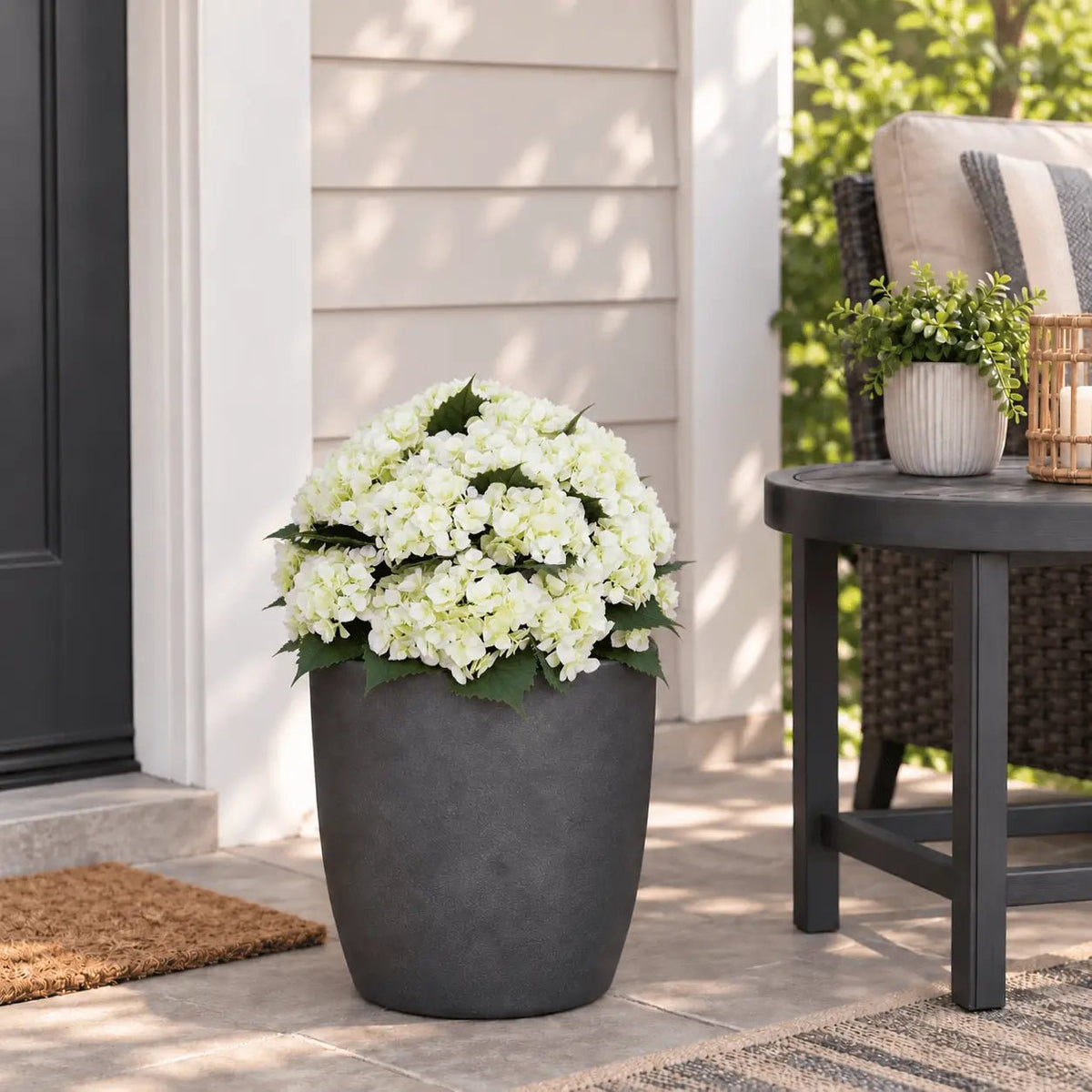 White artificial hydrangea bush seated low in an outdoor planter with the planting stake fully concealed