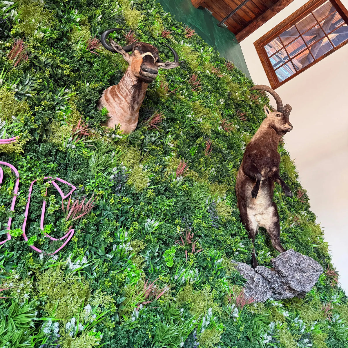 Amazon Jungle Artificial Vertical Garden Green Wall Panel 40×40in 11 SQ FT UV Resistant Commercial Grade installed as a large indoor feature wall with mounted wildlife displays, neon signage, and layered tropical greenery in a commercial venue.