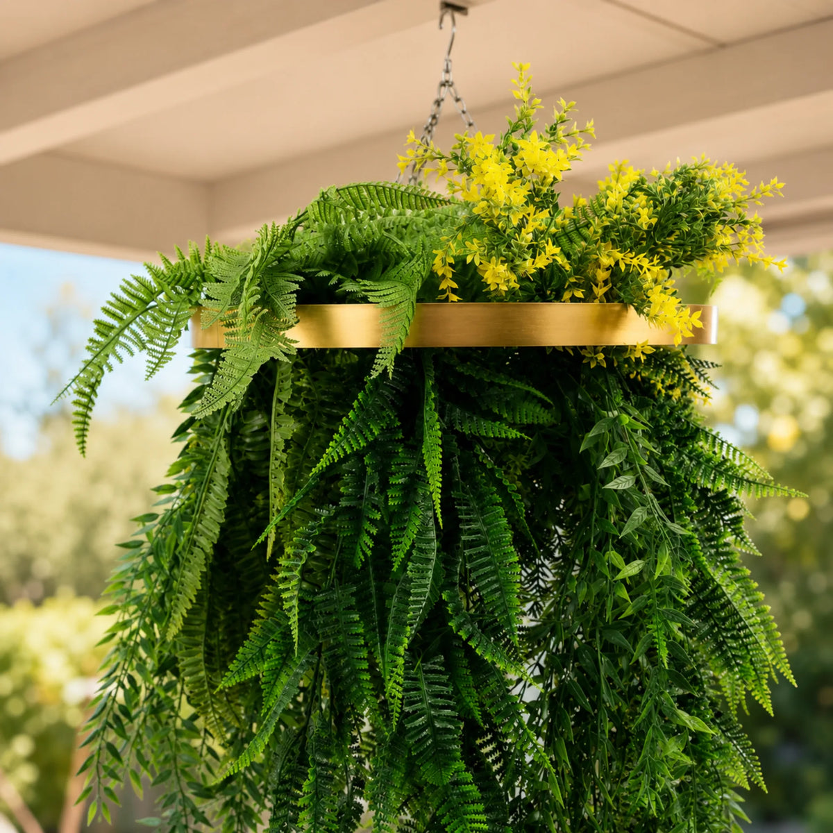 Close-up of an artificial hanging plant chandelier with a gold circular ring frame, bright tropical foliage, cascading fern greenery, and yellow floral accents with UV resistant leaves.
