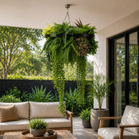 UV resistant black framed hanging plant chandelier with tropical foliage and cascading greenery suspended above a stylish outdoor patio seating area in bright natural light.