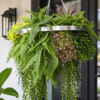 Close-up of a silver framed artificial hanging plant chandelier featuring lush tropical foliage, layered fern leaves, trailing greenery, and delicate floral accents suspended by metal chains.