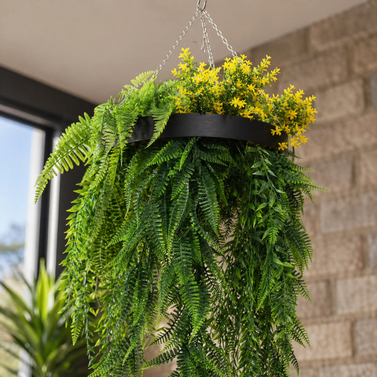 Close-up of a black framed artificial hanging disc featuring bright tropical foliage, cascading fern leaves, and yellow floral accents with a UV resistant finish.