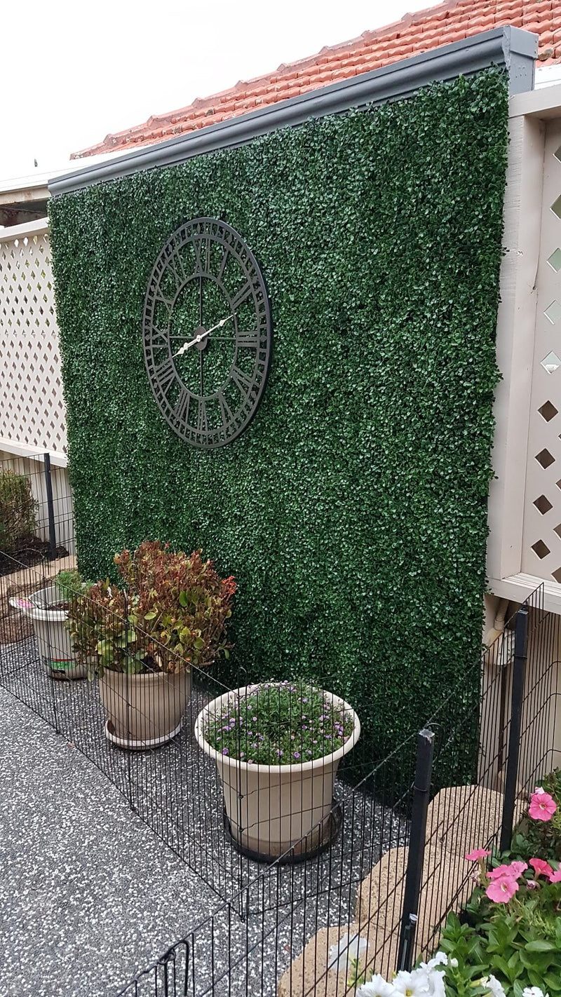 Faux Boxwood Hedge Panels Installed Along a Fence with a Large Outdoor Clock