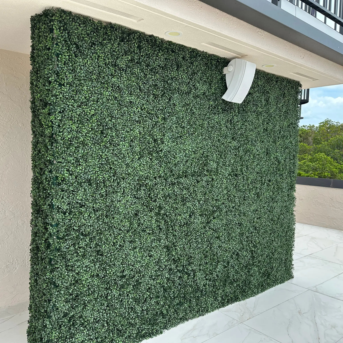 Angled close-up of Dark Boxwood Artificial Vertical Garden Green Wall Panel with rich dark green foliage, installed on a modern balcony wall to enhance privacy and add a lush contemporary greenery feature.