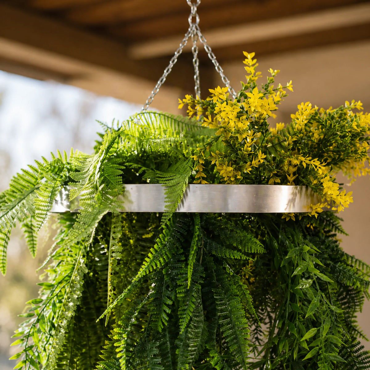 Close-up of a silver framed hanging disc arrangement featuring cascading fern greenery, tropical foliage, and bright yellow floral accents with UV resistant artificial plants.