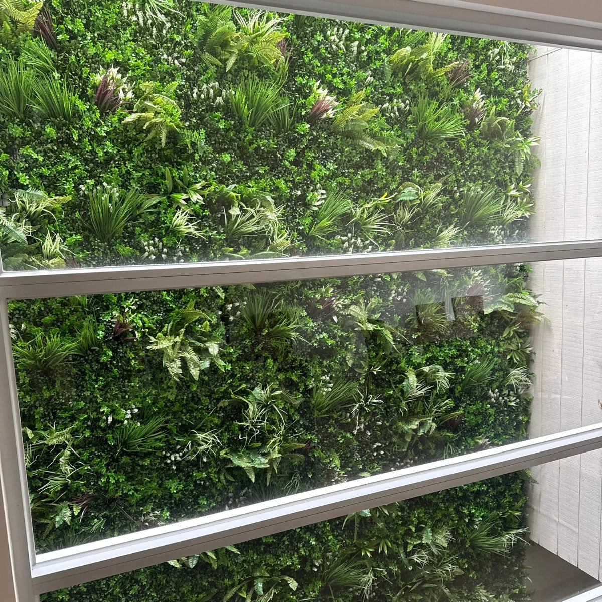 View through a window with horizontal bars looking out onto a lush vertical garden wall filled with dense green foliage and varied plants.