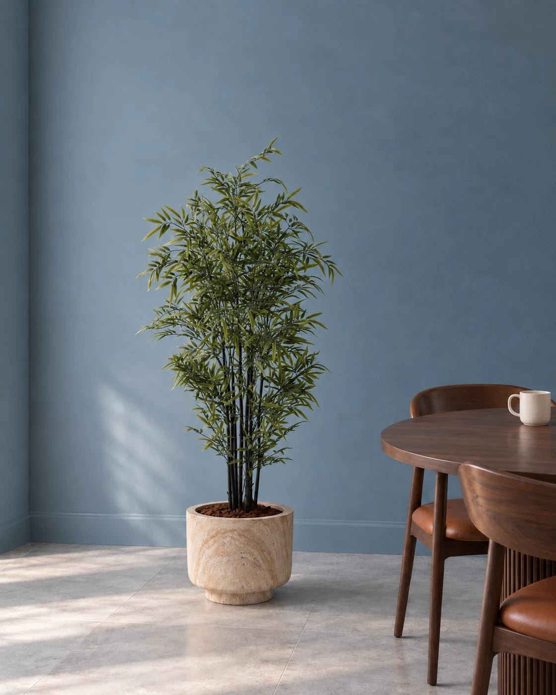 150 cm artificial Black Bamboo in a marble-effect pedestal planter beside walnut dining furniture against a muted blue wall.