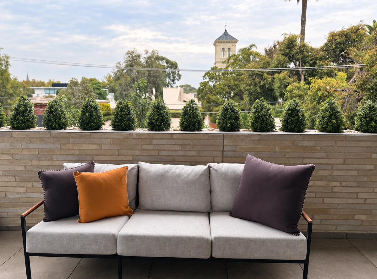 Modern outdoor sofa with gray cushions and decorative pillows on a patio with greenery.