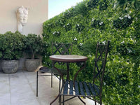 Small outdoor patio with a round table and two chairs surrounded by greenery.