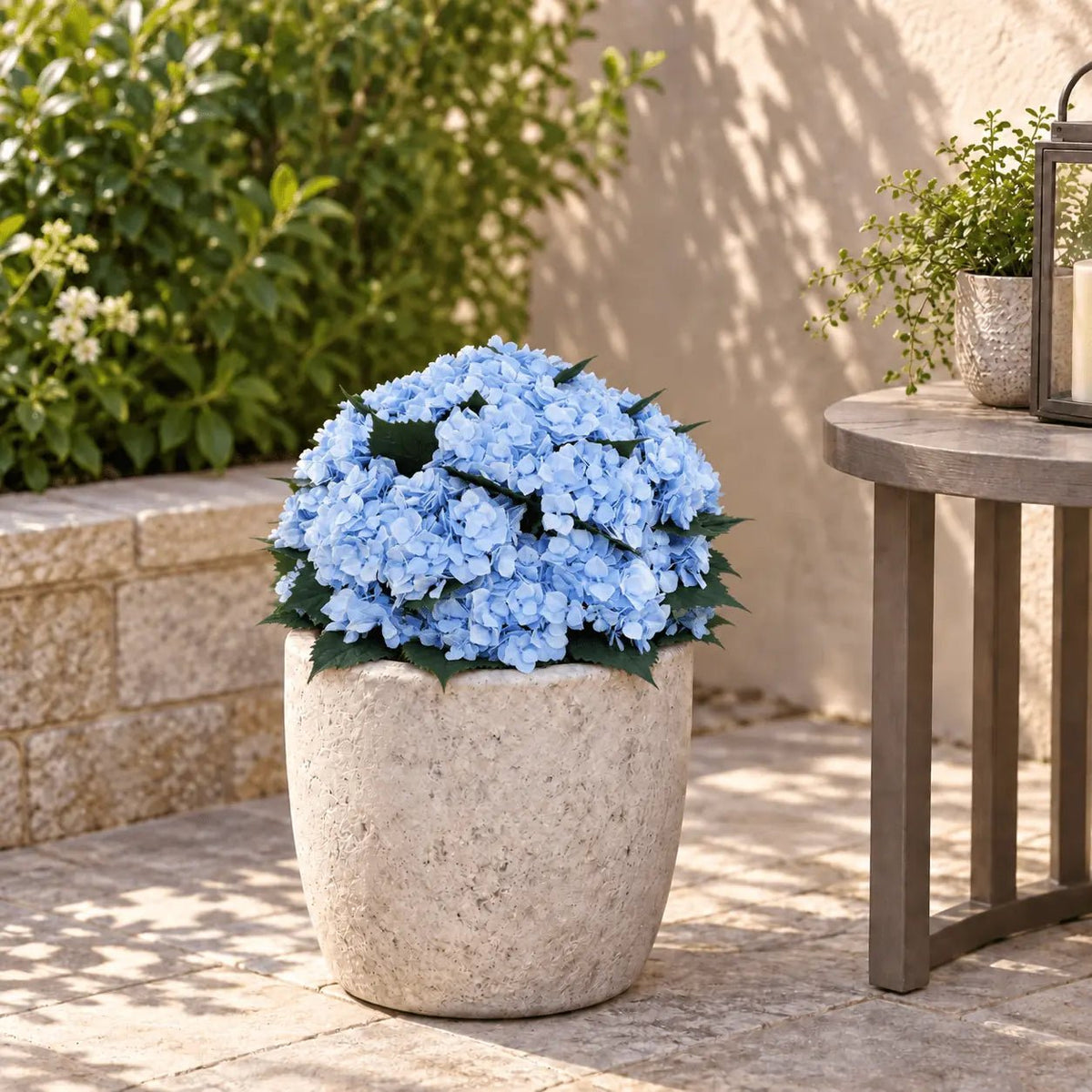 Blue artificial hydrangea bush seated low in an outdoor planter with the planting stake fully concealed