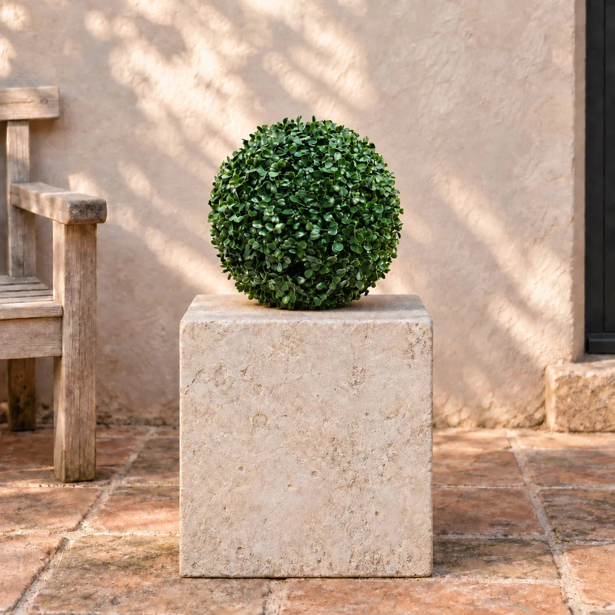 Artificial boxwood topiary ball displayed on a stone courtyard plinth