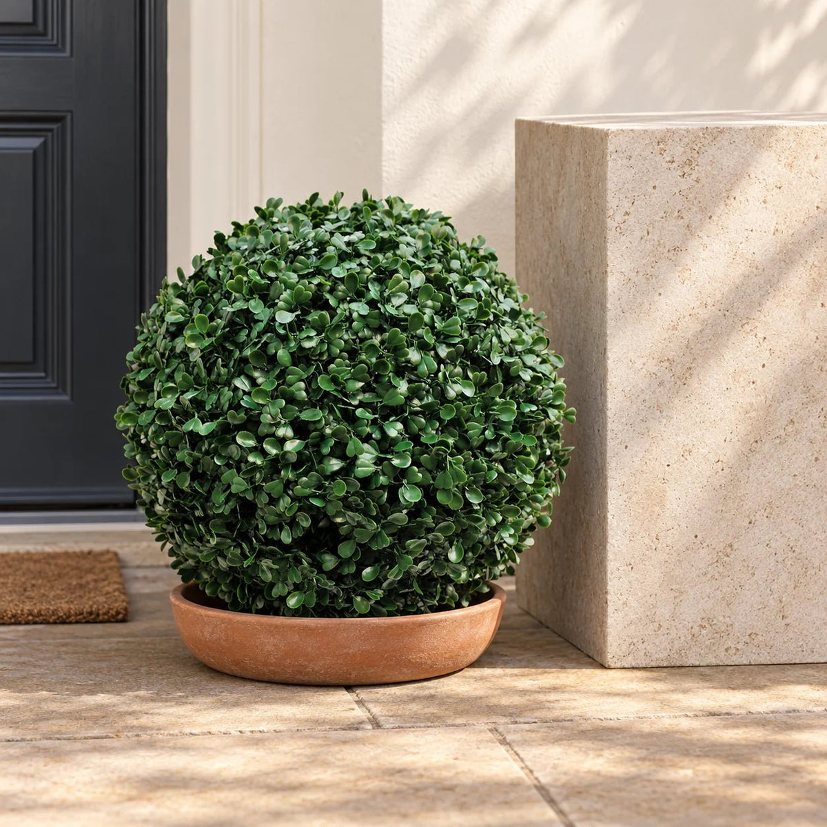 Artificial boxwood topiary ball in a low bowl on a sheltered porch