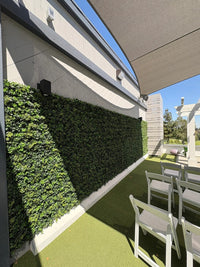 Outdoor patio area with greenery, chairs, and a clear sky.
